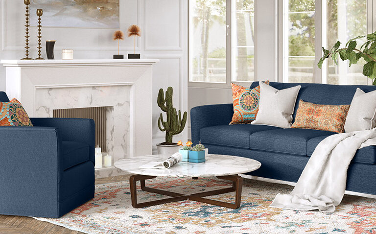 Clarissa collection by Vogel next to a fireplace - upholstered in navy fabric and accented with white and orange throw pillows and a colourful area rug