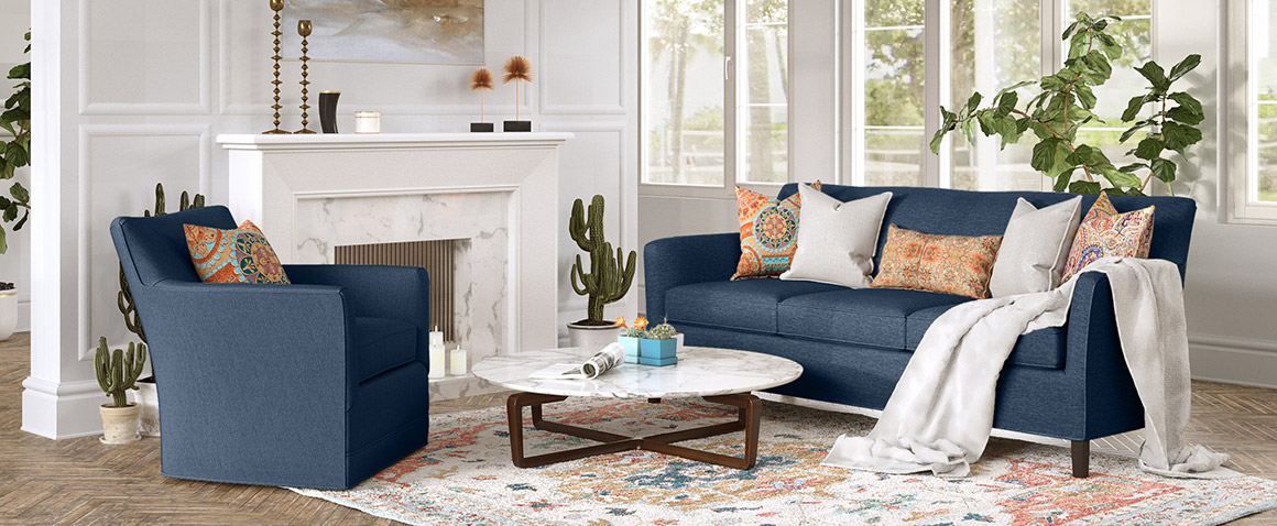 Clarissa collection by Vogel next to a fireplace - upholstered in navy fabric and accented with white and orange throw pillows and a colourful area rug
