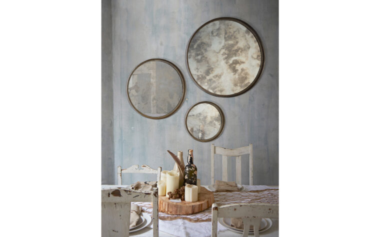 Shire Mirror Collection - Renwil - decorative collection of circular antique mirrors with antiqued frames; collection hanging on rustic grey wall behind distressed, farmhouse-style dining room table and chairs (candles, old wine bottles, feather, and slab of wood used to create centrepiece)
