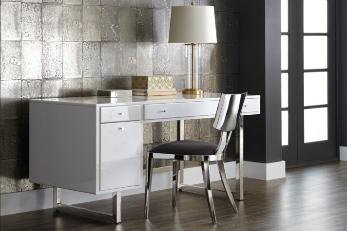 White desk with small and large drawers with an office chair, lamp, and decor. 