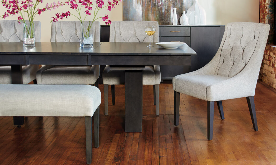 A solid wood dining table in a dark grey stain with beige upholstered chairs and a bench