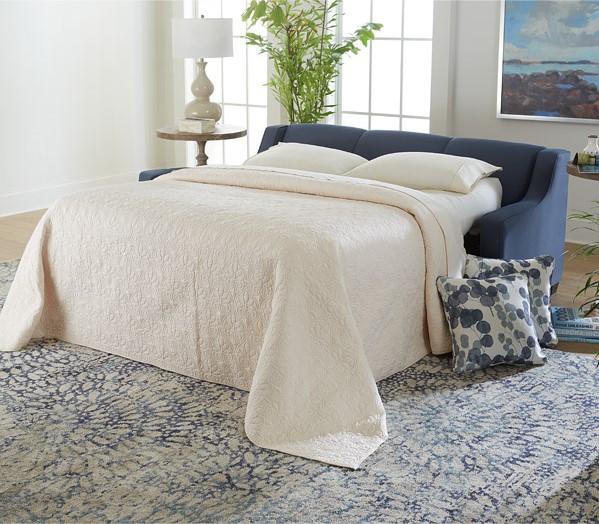 A sofa bed in a living room setting that has the bed open and made, ready for a guest to rest on. 