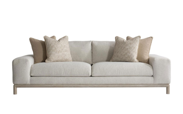 The sleek, modern Hadley sofa with a light wood frame shown in a cream fabric with 2 brown and beige throw pillows on either side
