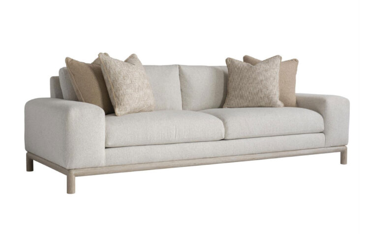Angled view of the sleek, modern Hadley sofa with a light wood frame shown in a cream fabric with 2 brown and beige throw pillows on either side