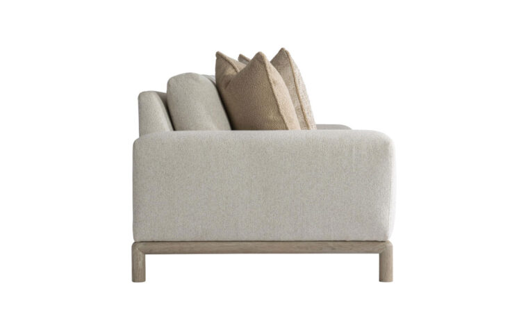 Side view of the sleek, modern Hadley sofa with a light wood frame shown in a cream fabric with 2 brown and beige throw pillows on either side
