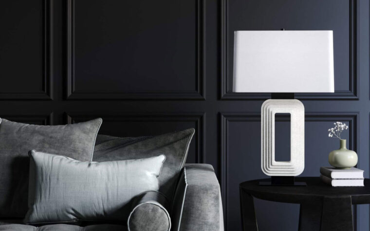 Modern stone table lamp with rectangular ivory composite base with hollow centre and etched pattern on a side table in a dark, moody living room