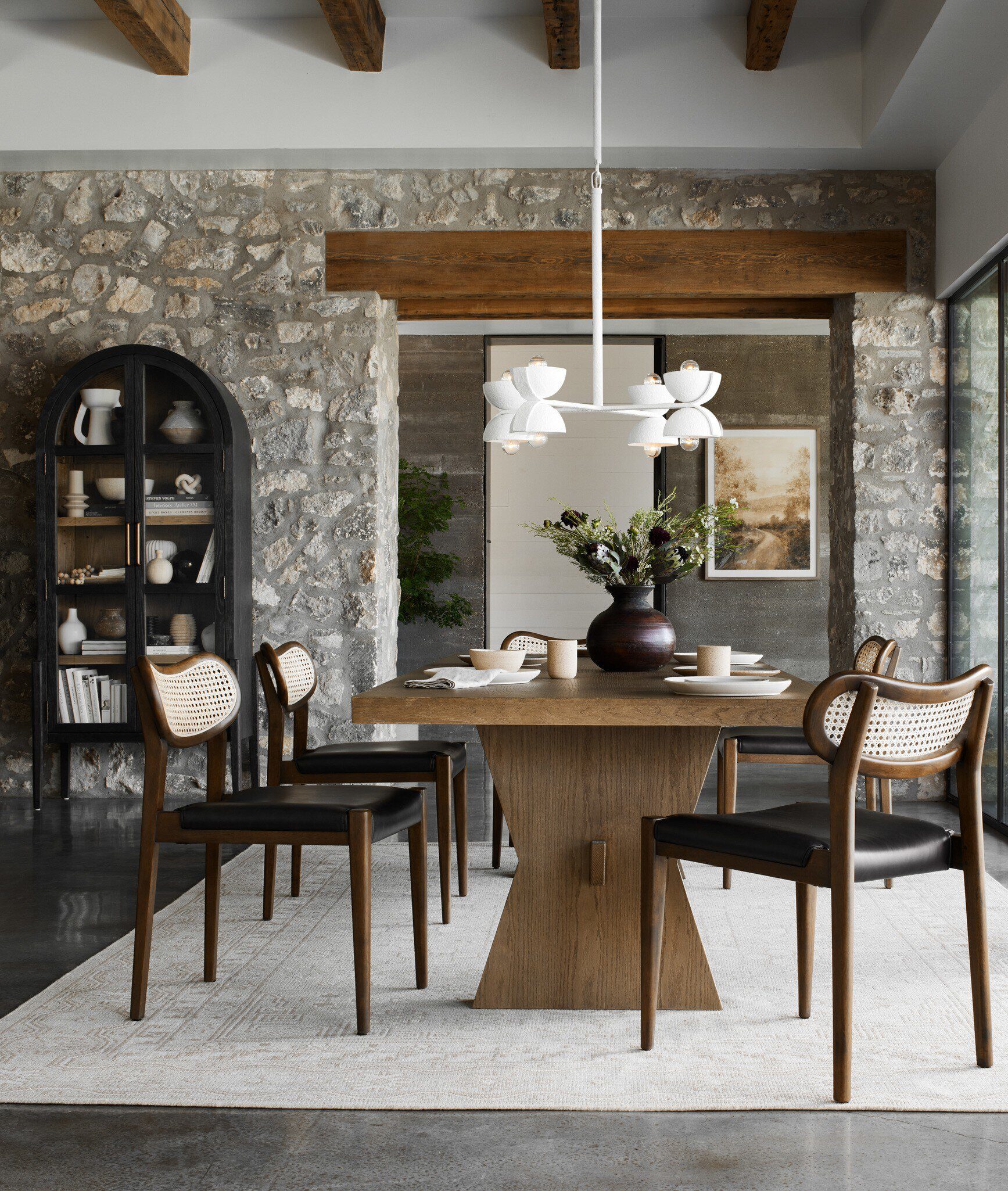 A black arched bookcase with drifted oak interiors in a dining room setting by Four Hands.