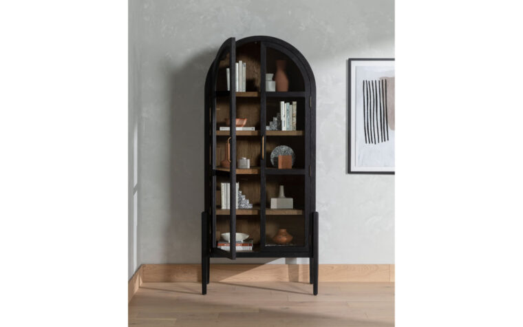 A black arched bookcase with drifted oak interiors in a room setting by Four Hands.