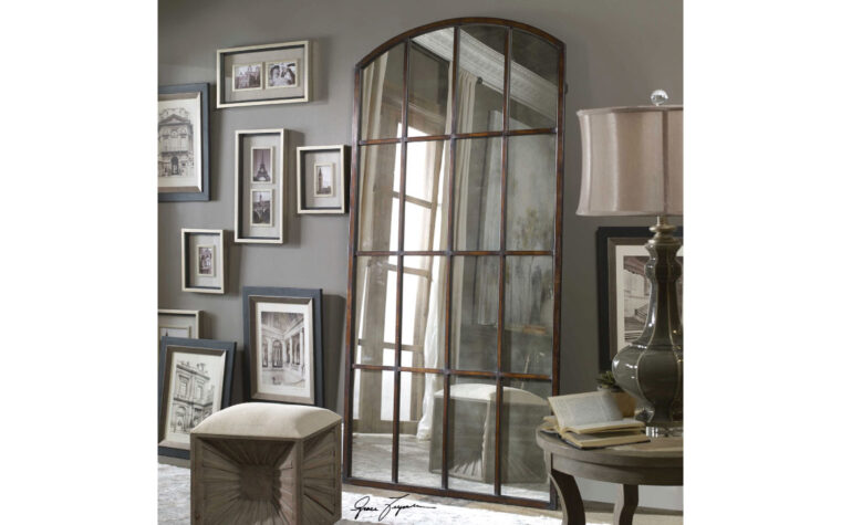 Large Arch Mirror in bronze with paneling by Uttermost leaning against a wall.