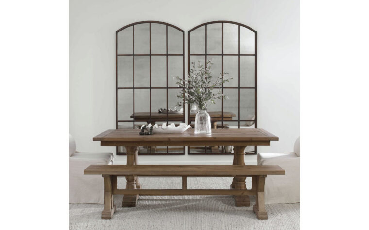Large Arch Mirror in bronze with paneling by Uttermost hanging on a wall behind a dining room table.