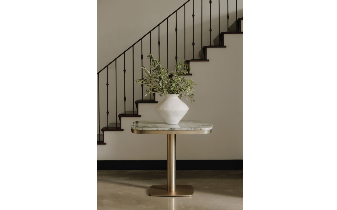 Green marble cafe table with brass base in front of staircase with a vase on top.